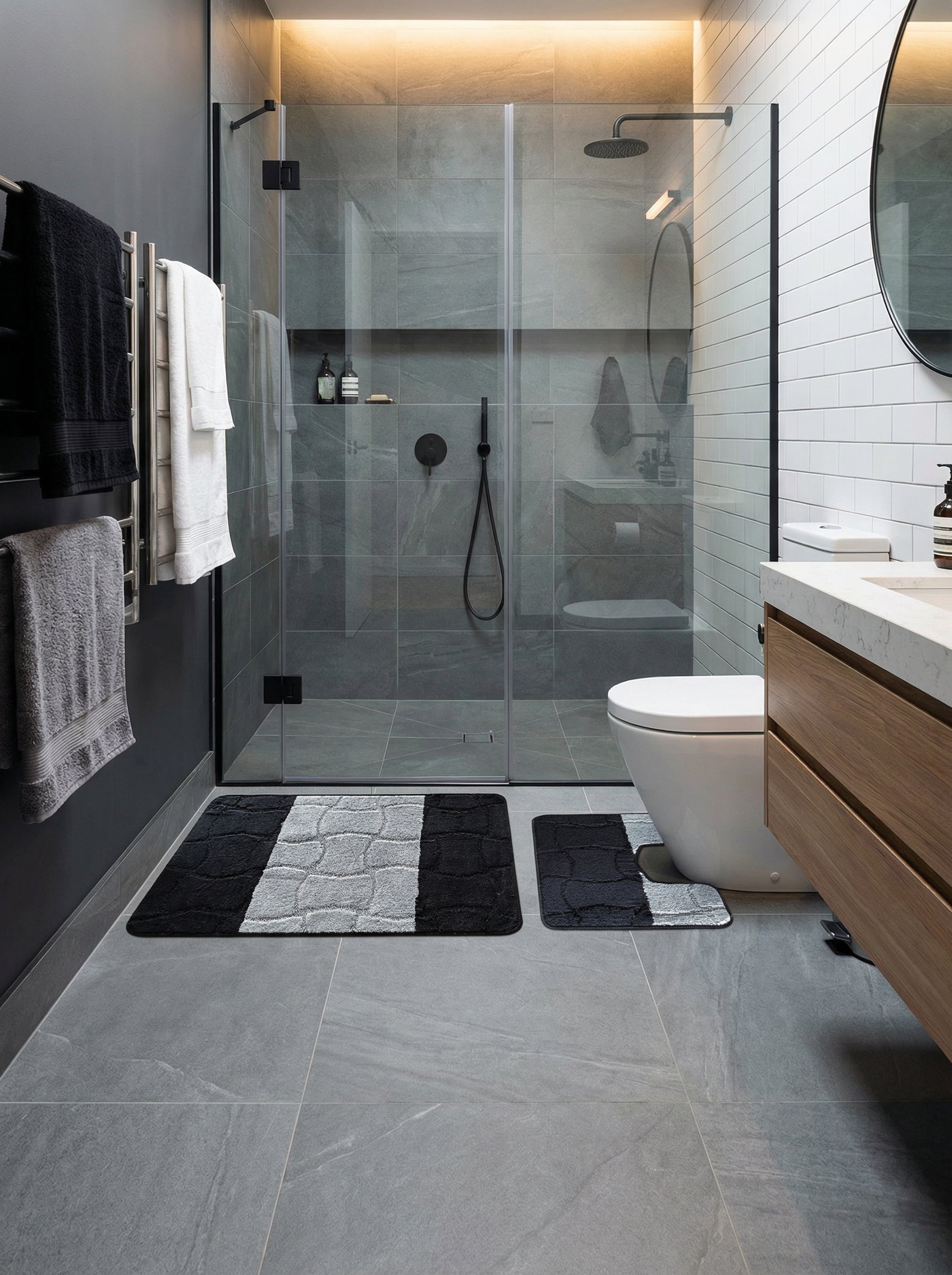 Ensemble de tapis de bain noirs et gris clair à motifs texturés, disposés sur le sol carrelé d'une salle de bain moderne