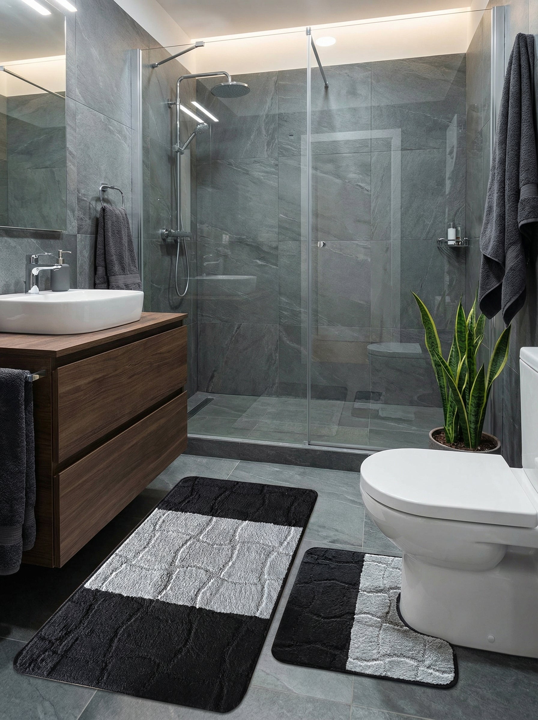 Deux tapis de bain, un rectangulaire et un en U, noirs et gris clair avec des motifs de pavés texturés, dans une salle de bain moderne