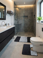 Deux tapis de bain noirs et gris clair, un rectangulaire et un en forme de U, avec un motif de galets texturés, dans une salle de bain moderne