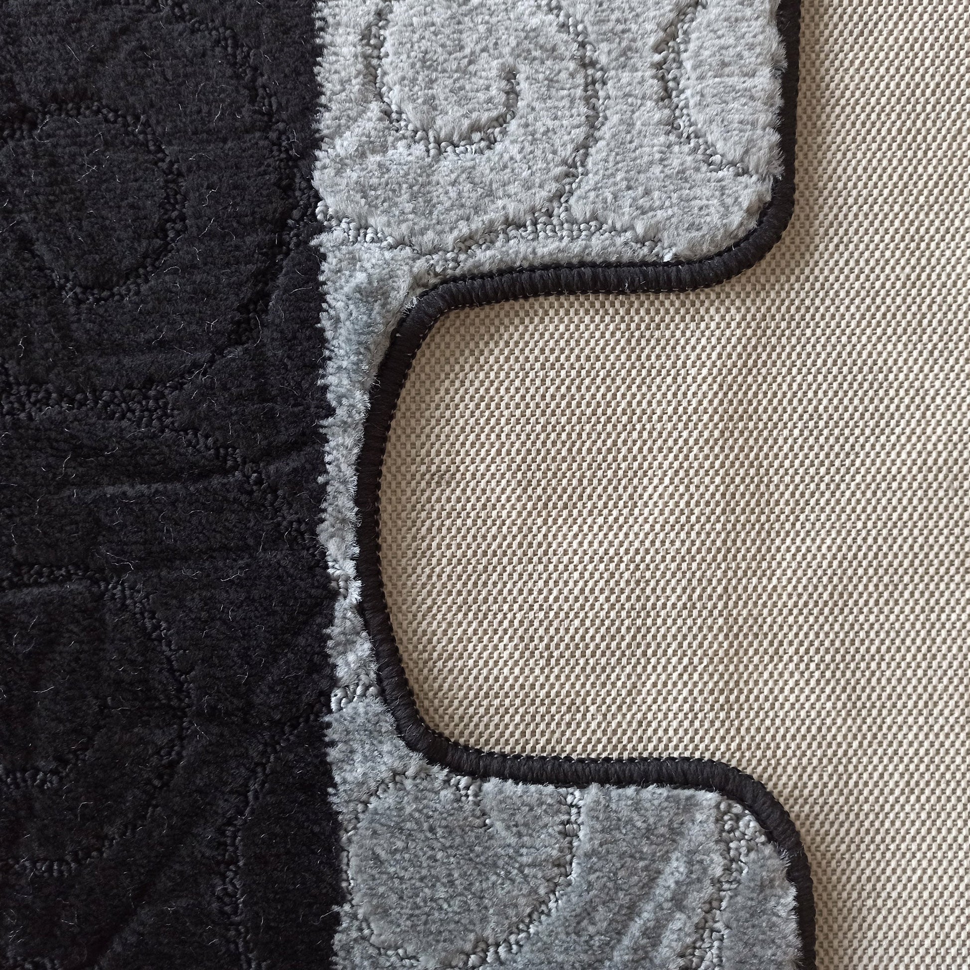 Tapis moelleux bicolore noir et gris clair avec des motifs en relief et une bordure foncée, l'envers tissé est visible