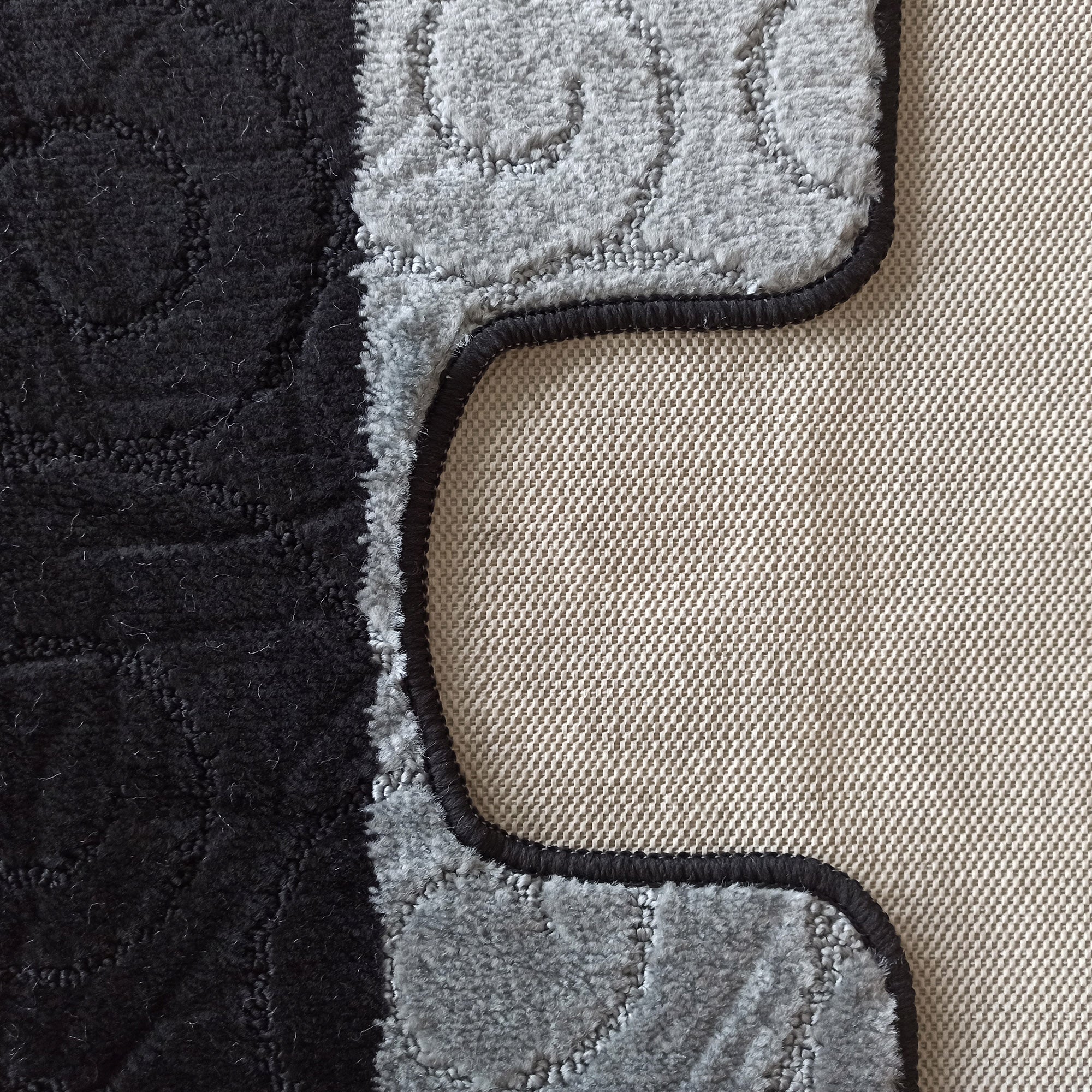 Tapis moelleux bicolore noir et gris clair avec des motifs en relief et une bordure foncée, l'envers tissé est visible