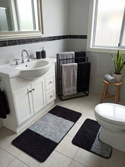 Tapis de bain noir et gris clair à motifs de volutes texturées, l'un rectangulaire et l'autre en U autour des toilettes, dans une salle de bain