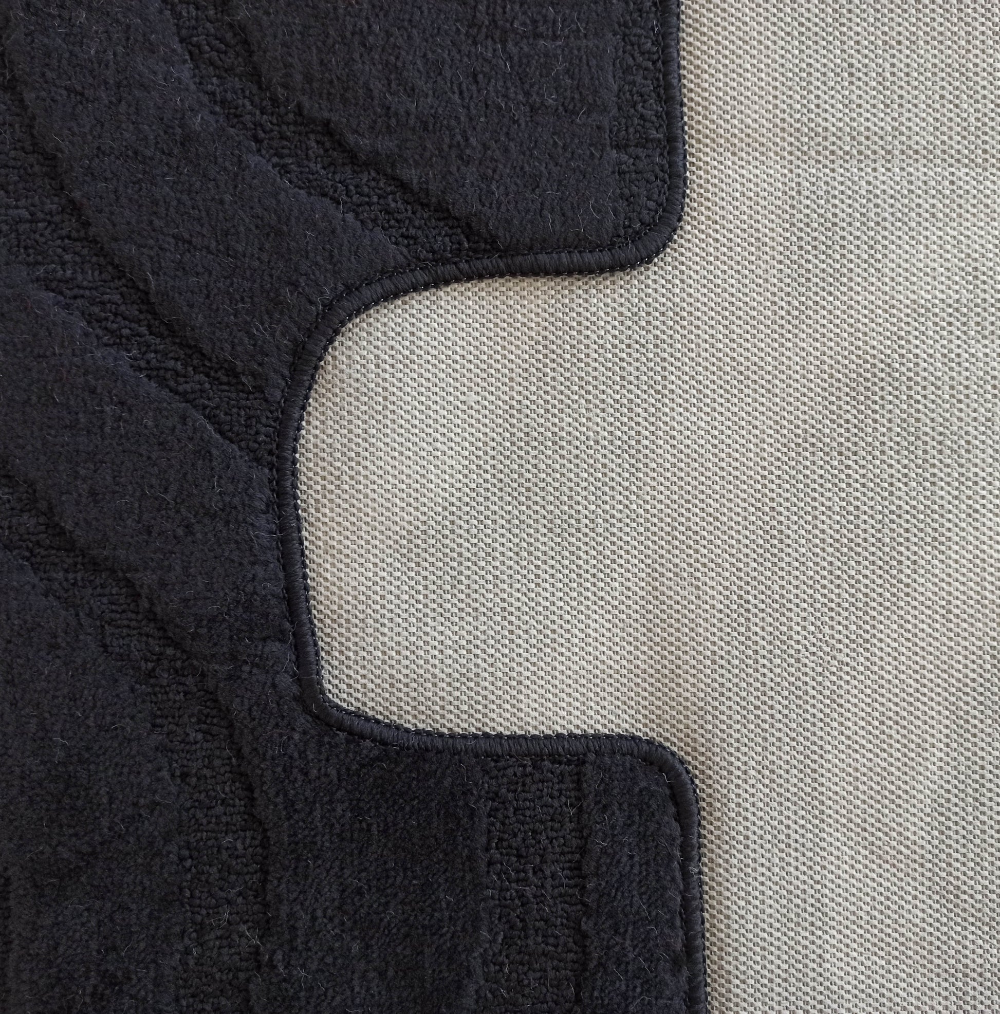 Tapis noir à la texture bouclée, bordé d'un motif tissé gris clair en grille avec une ligne courbe