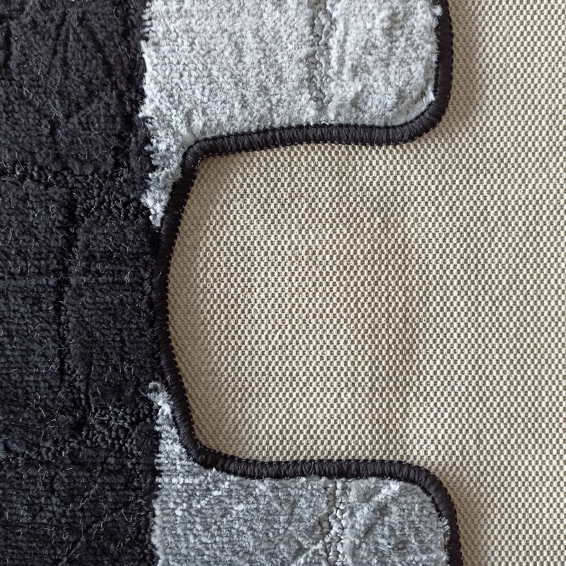 Gros plan sur un tapis texturé noir et gris clair, avec un motif ondulé, et son envers beige tissé à petits carreaux