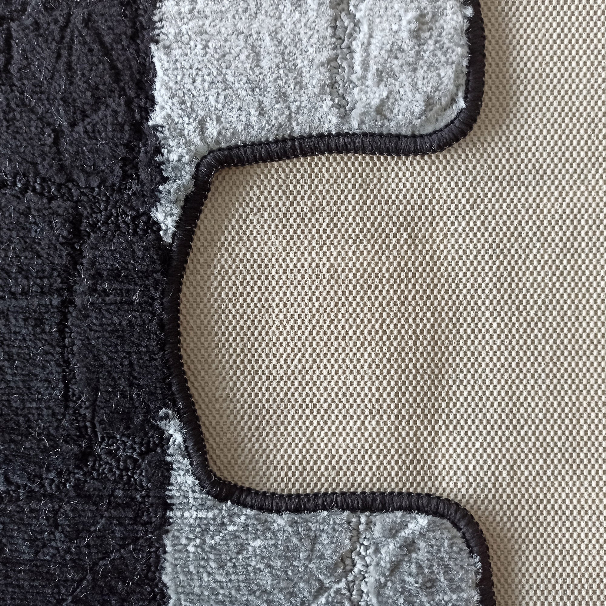 Gros plan sur un tapis texturé noir et gris clair, avec un motif ondulé, et son envers beige tissé à petits carreaux