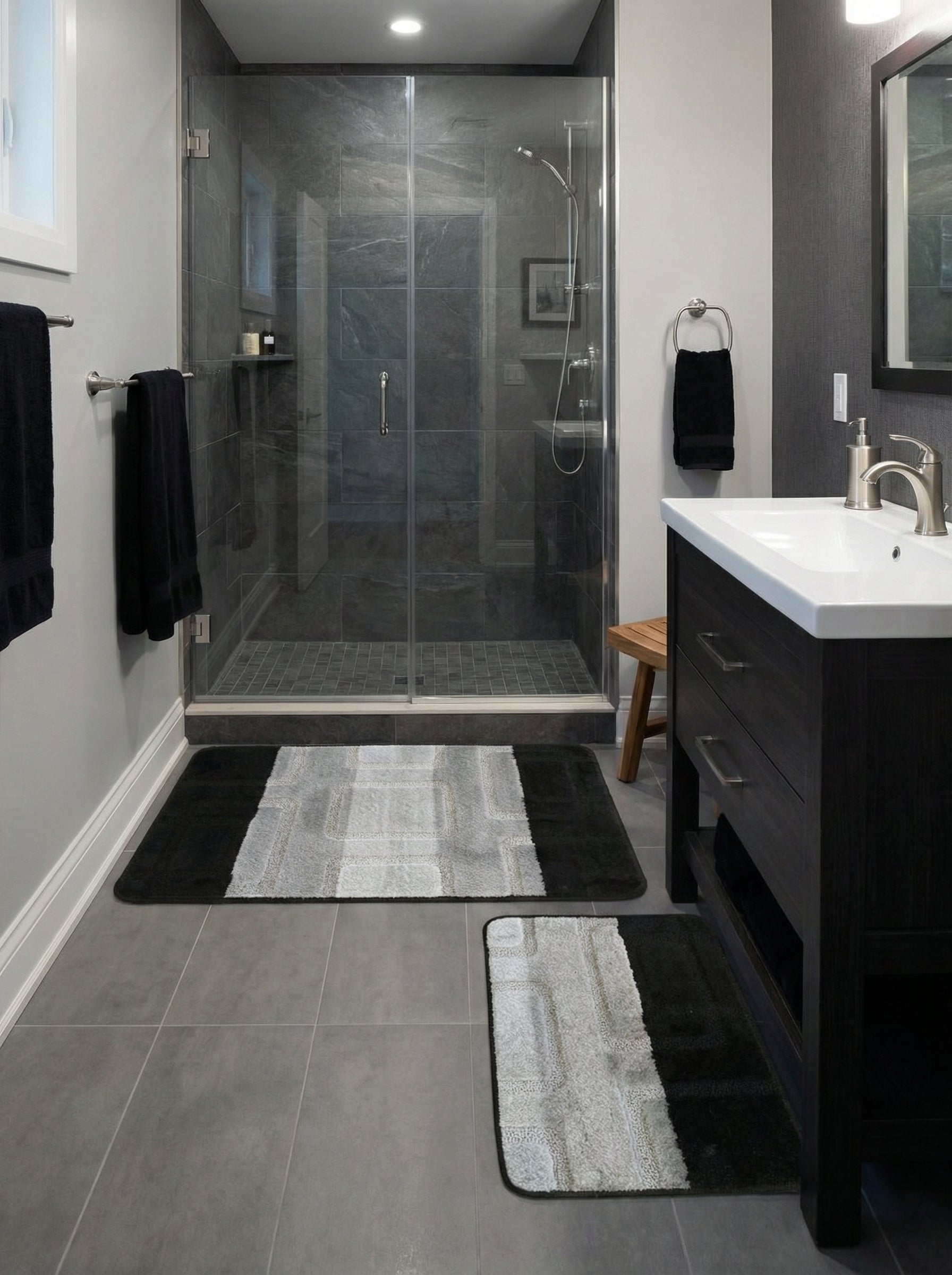 Deux tapis de bain moelleux rectangulaires, noirs et gris clair à motifs géométriques, dans une salle de bain carrelée