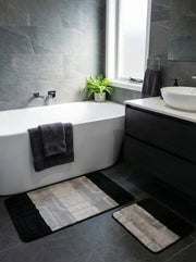 Deux tapis de bain rectangulaires, gris clair, beige et noir à motifs géométriques, sur un carrelage de salle de bain