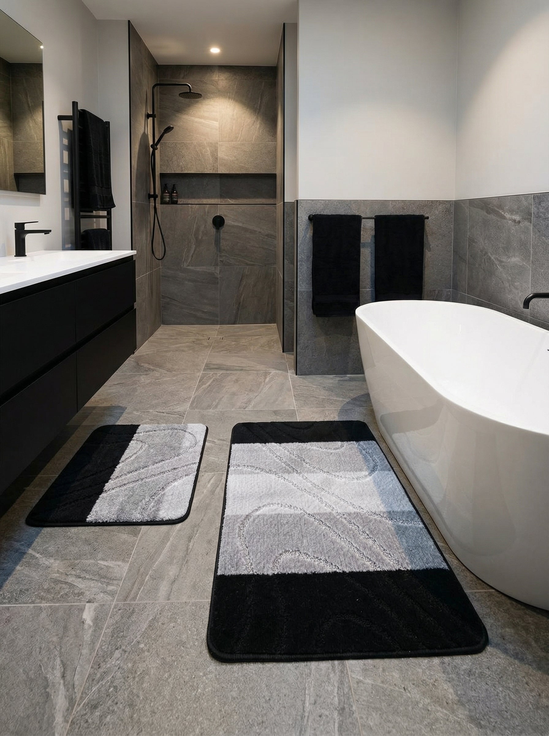 Deux tapis de bain rectangulaires moelleux gris et noirs avec des motifs ondulés, posés sur un sol carrelé dans une salle de bain moderne