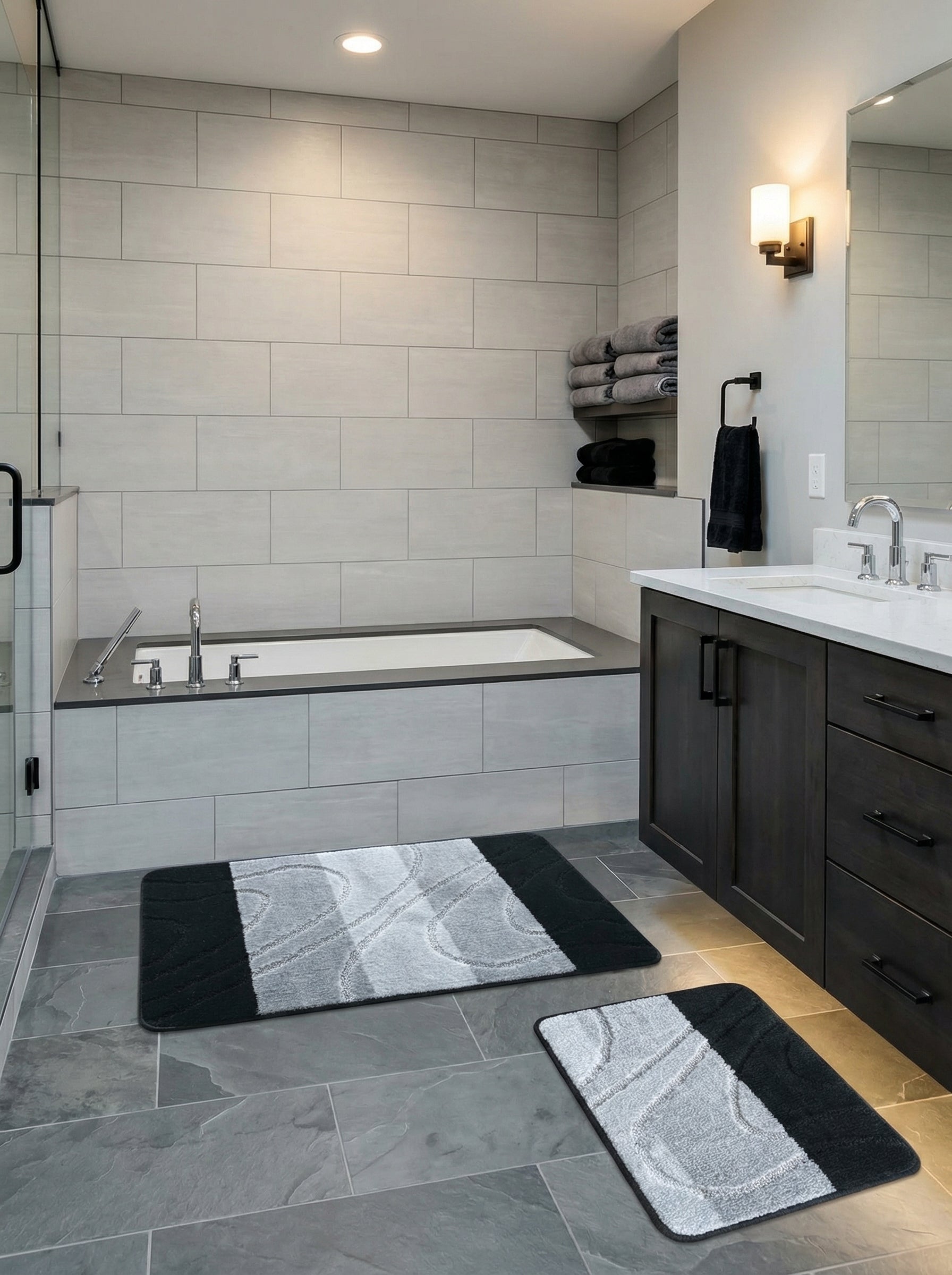 Deux tapis de bain rectangulaires doux, noirs et gris à motifs ondulés texturés, dans une salle de bain moderne