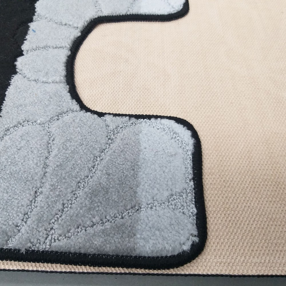 Gros plan d'un tapis aux motifs gris duveteux et matelassés, avec un contour noir sur une base beige tissée texturée