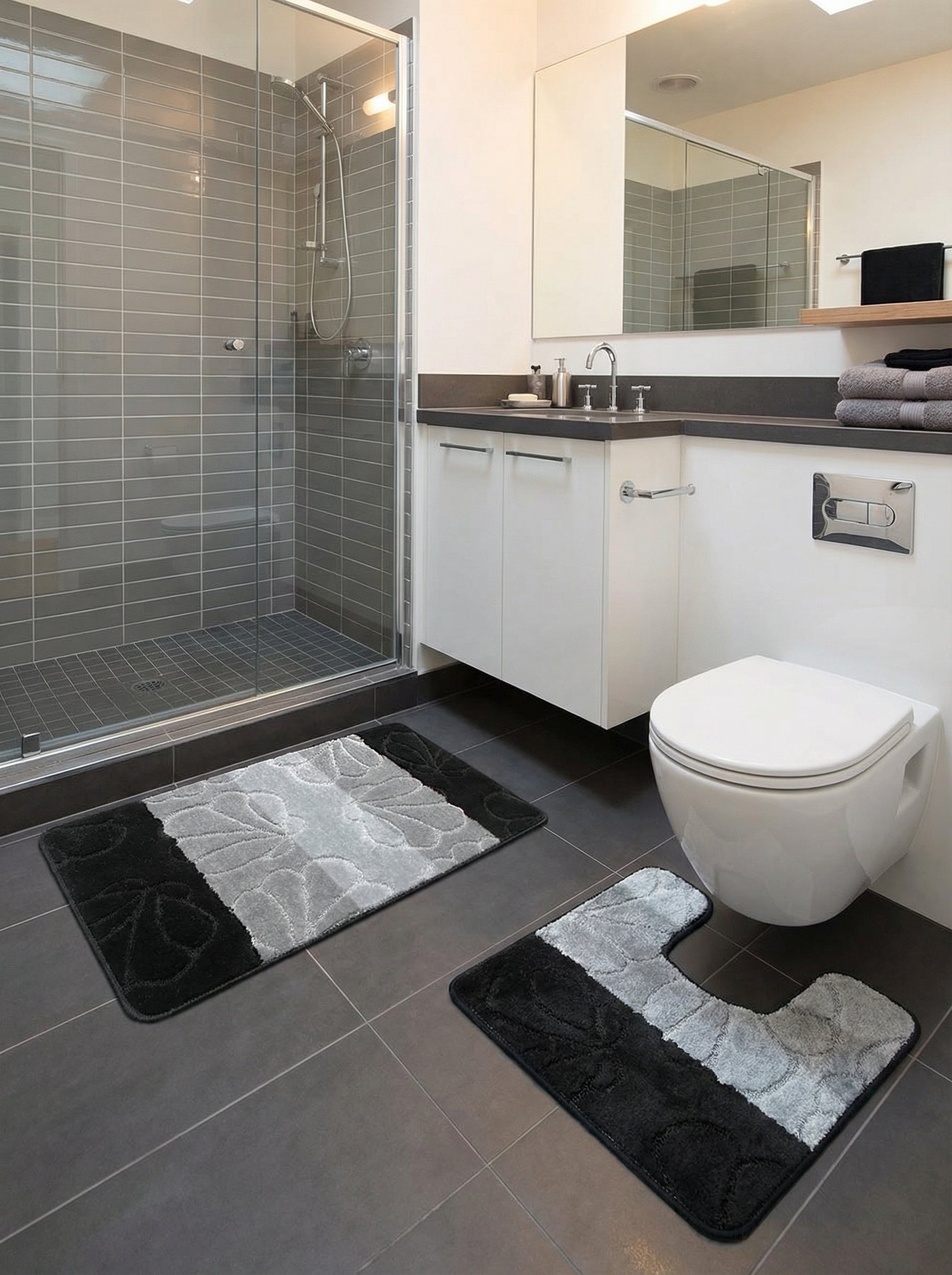 Deux tapis de bain moelleux, gris clair et noir avec des motifs floraux en relief, un rectangulaire et un en U, dans une salle de bain moderne