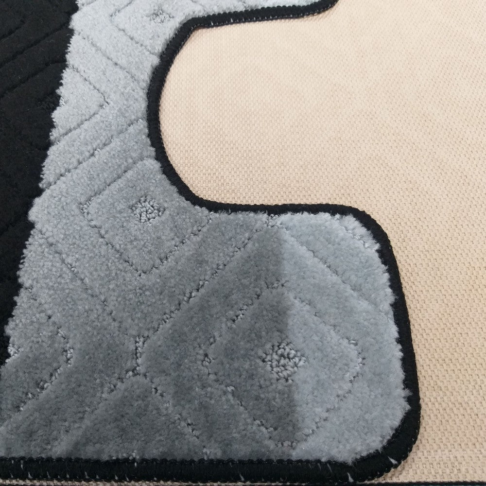 Tapis bicolore gris et noir, orné de motifs de losanges en relief. Une bordure noire souligne ses contours sur un fond beige