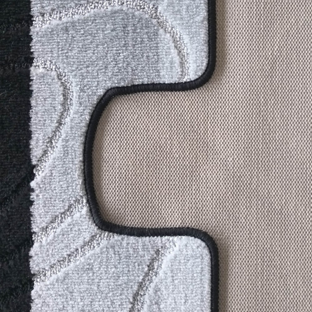 Tapis gris clair moelleux aux motifs ondulés subtils, bordé de noir et posé sur un revêtement beige tissé