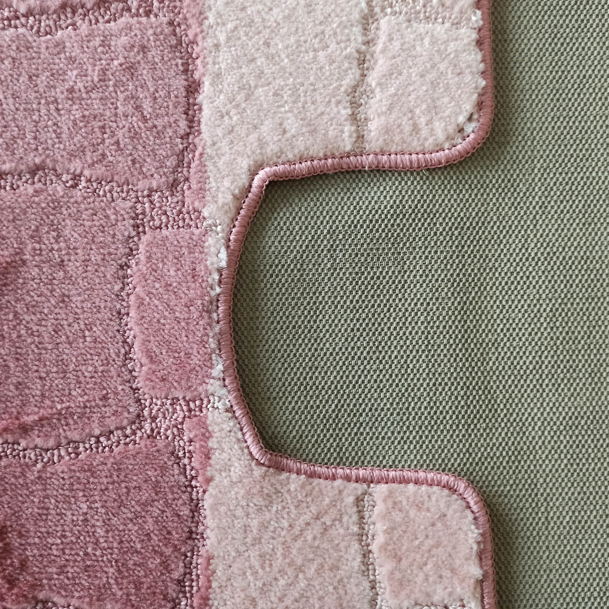 Tapis rose en relief avec des carrés de différentes teintes de rose clair et foncé, bord ondulé sur un textile vert