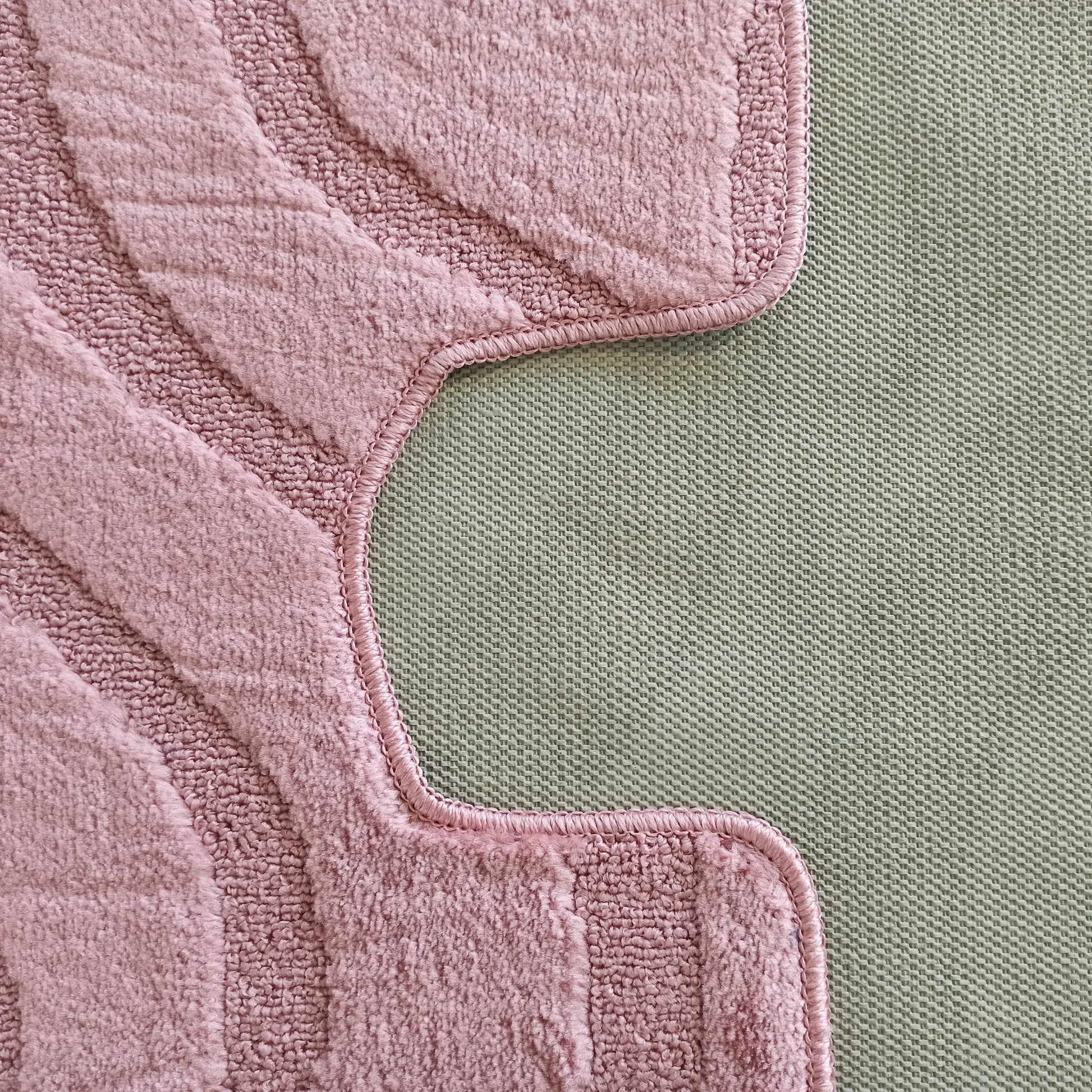 Tapis rose poudré à la texture moelleuse et motifs ondulés en relief. Sa bordure surjetée repose sur un fond vert tissé