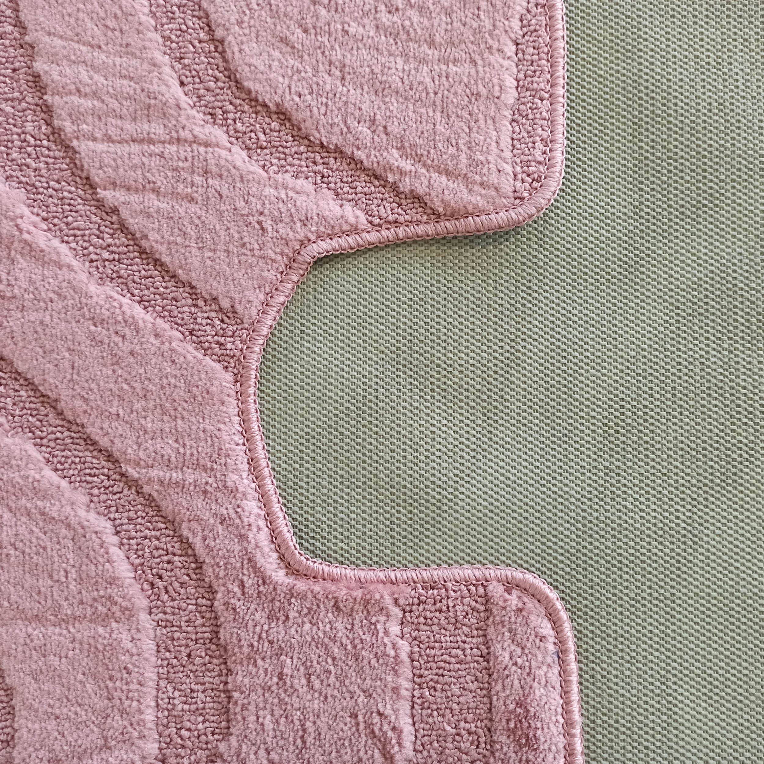 Tapis rose poudré à la texture moelleuse et motifs ondulés en relief. Sa bordure surjetée repose sur un fond vert tissé