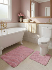 Deux tapis de bain roses texturés avec des motifs ondulés, un rectangulaire et un en U, dans une salle de bain aux tons roses