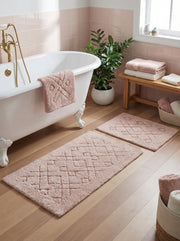 Deux tapis rectangulaires rose pâle en bouclette à motifs géométriques en relief, posés au sol d'une salle de bain