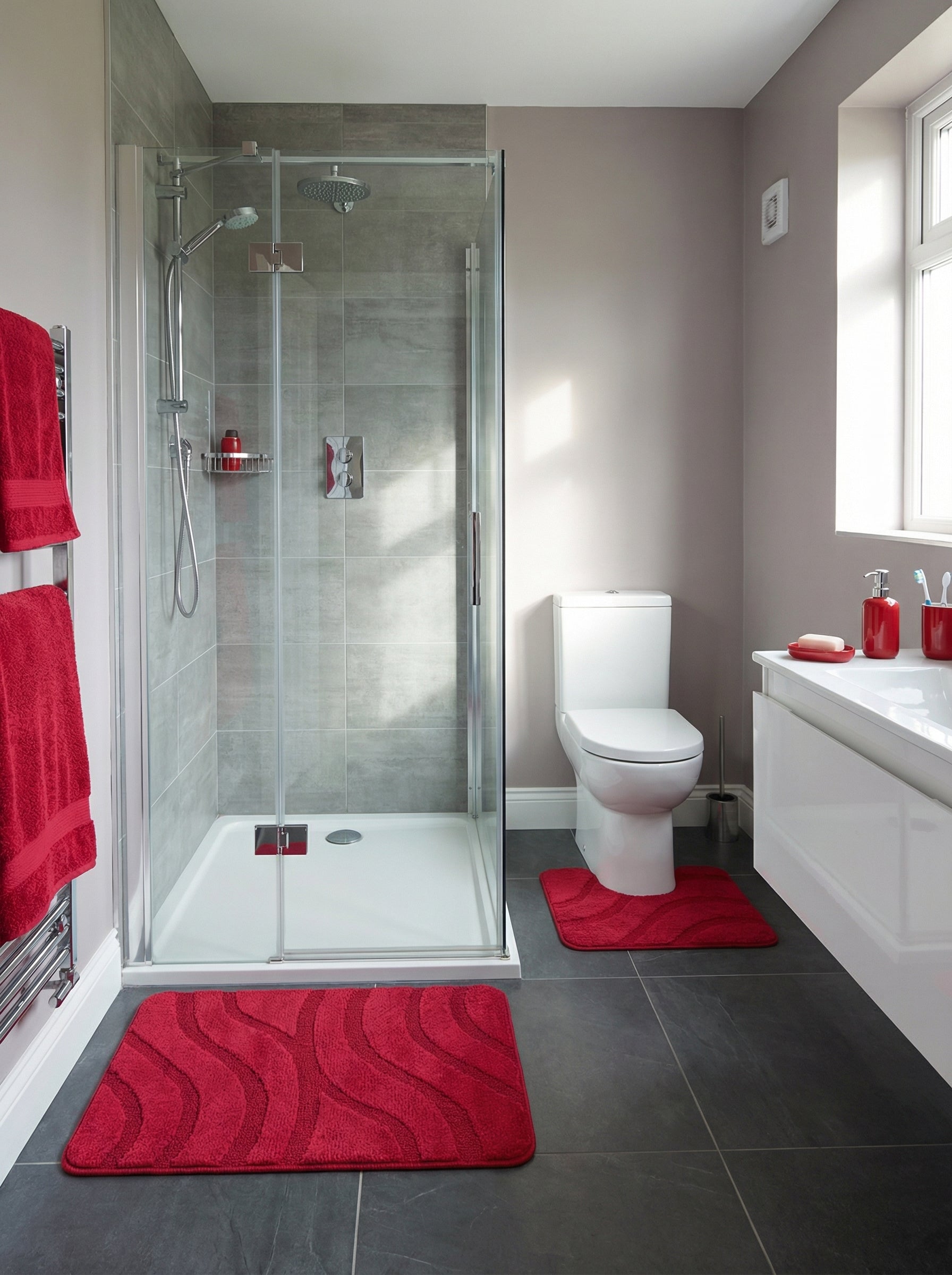 Grand tapis de bain rouge vif aux motifs ondulés texturés, posé sur un sol carrelé gris foncé dans une salle de bain moderne