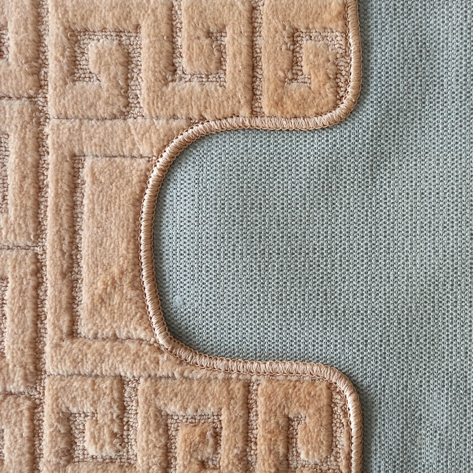 Tapis beige clair à texture douce avec motifs de méandres en relief, bordé d'un liseré incurvé sur son dos gris texturé