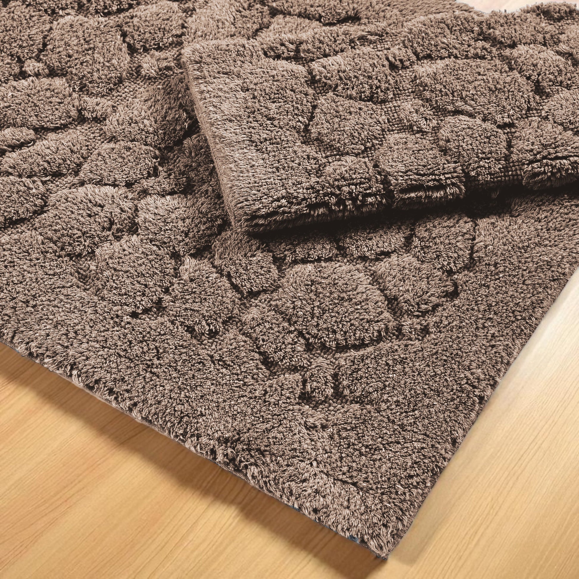 Tapis marron à texture bouclée et motif en relief de formes arrondies, sur un plancher en bois clair