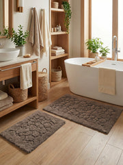Tapis de bain rectangulaires en tissu éponge marron aux motifs de galets en relief, sur le sol d'une salle de bain