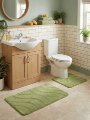 Deux tapis de bain rectangulaires verts clair, l'un découpé, avec des motifs ondulés en relief, sur le sol carrelé d'une salle de bain