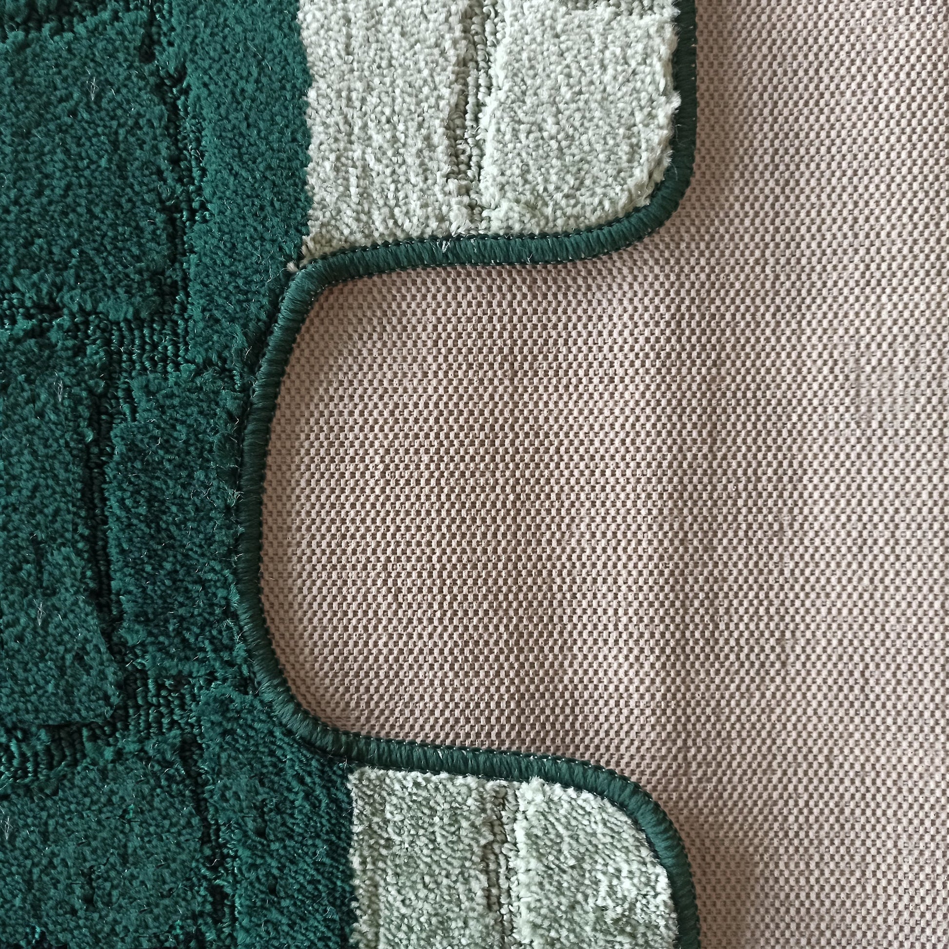 Tapis aux tons verts, foncé et clair, à texture bouclée, avec une bordure ondulée cousue sur un fond tissé beige