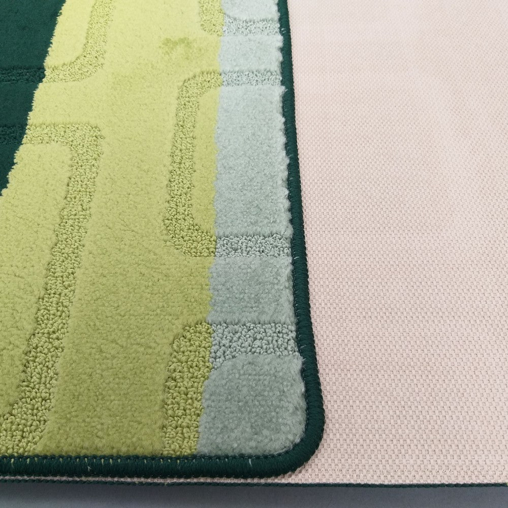 Tapis texturé aux motifs géométriques vert foncé, vert clair et bleu-gris, avec un liseré vert foncé et un dos beige