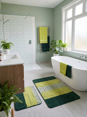 Deux tapis de bain moelleux aux motifs géométriques vert foncé et vert clair, posés sur le sol d'une salle de bain