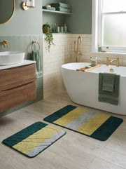 Deux tapis de bain rectangulaires moelleux vert foncé, jaune moutarde et gris clair à motifs ondulés sur le sol d'une salle de bain
