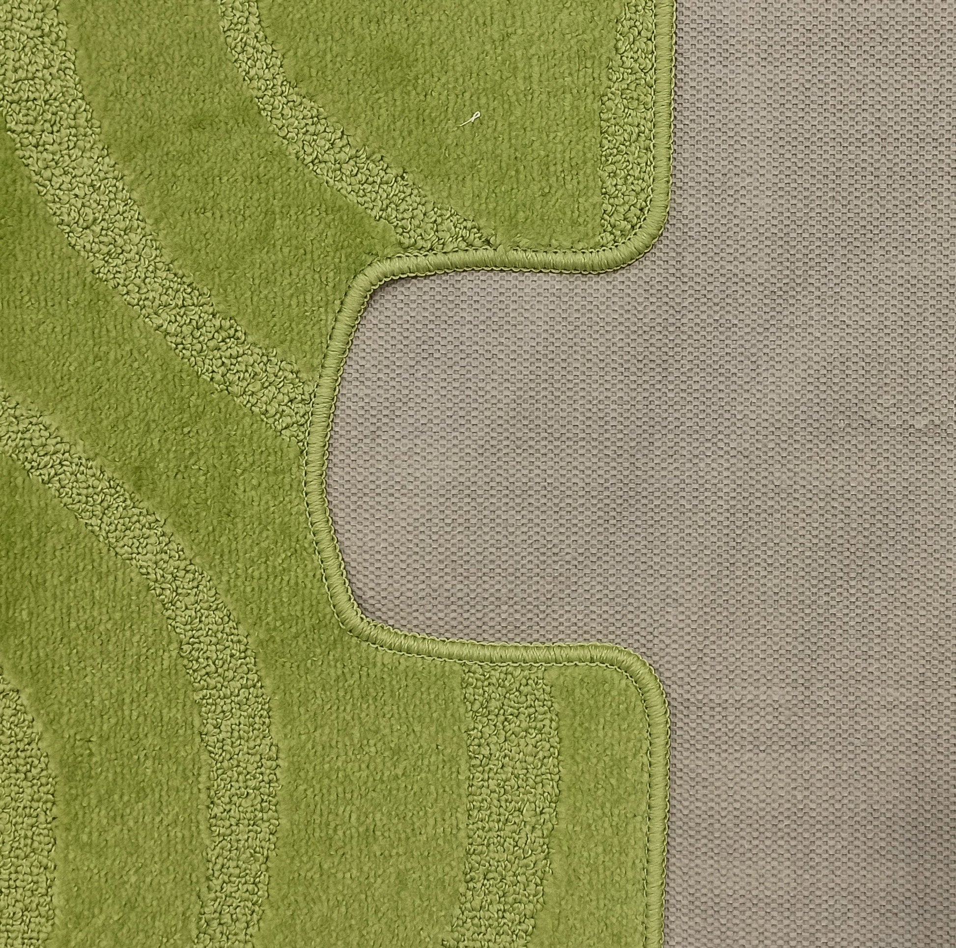 Tapis vert clair texturé, avec des bandes incurvées plus claires et un bord cousu, posé sur une surface grise