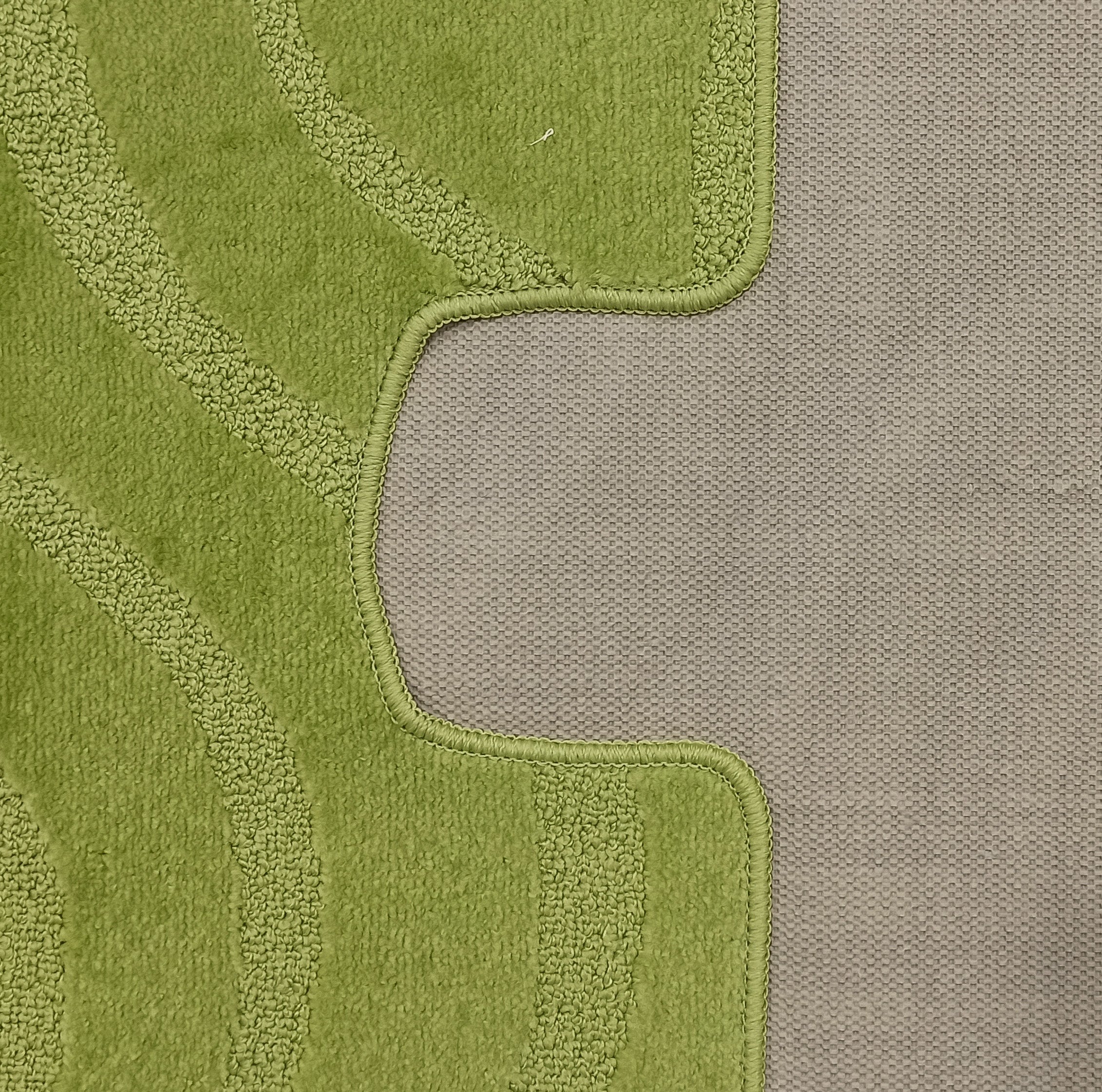 Tapis vert clair texturé, avec des bandes incurvées plus claires et un bord cousu, posé sur une surface grise