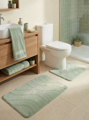 Tapis de bain vert clair rectangulaire et un autre en U avec motifs ondulés. Ils sont posés sur un carrelage beige dans une salle de bain moderne