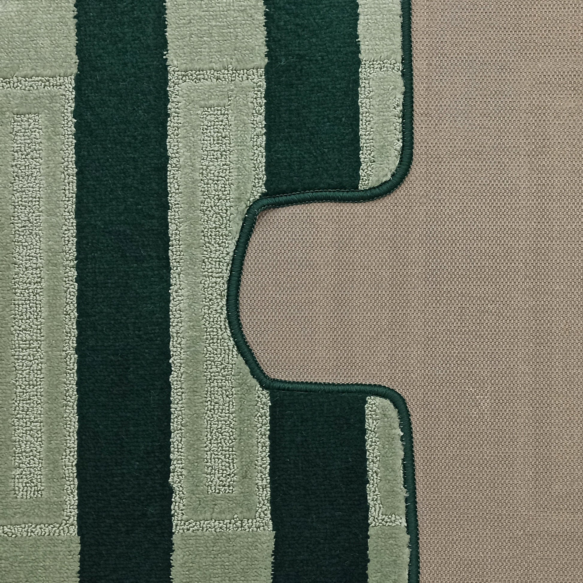 Tapis moelleux aux motifs géométriques vert foncé et vert sauge en relief, bordé d'une couture qui serpente sur un sol beige