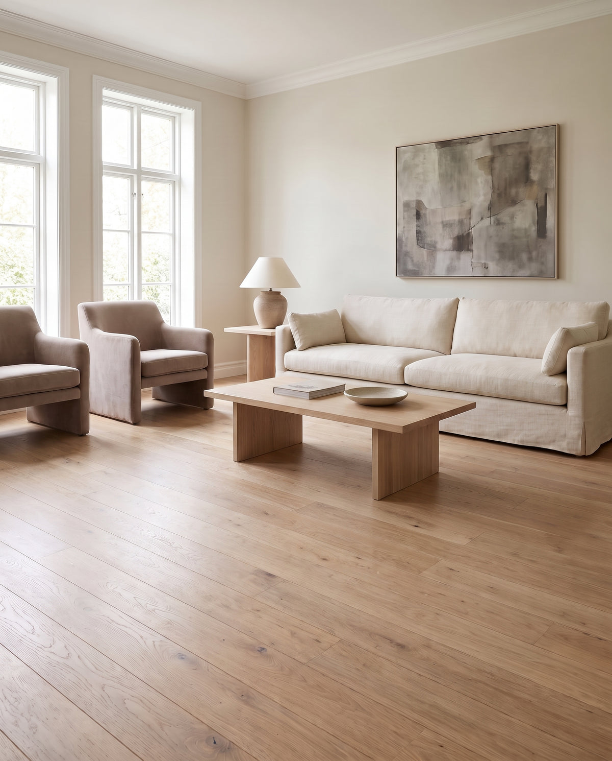 Salon moderne et lumineux, parquet clair, sans tapis, canapé beige, fauteuils taupe, table basse et tableau abstrait