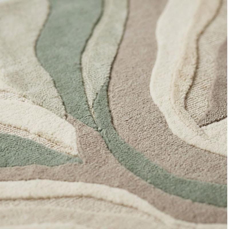 Relief détaillé des bandes ondulantes en laine beige et vert sauge, avec mèches coupées douces et bouclées texturées