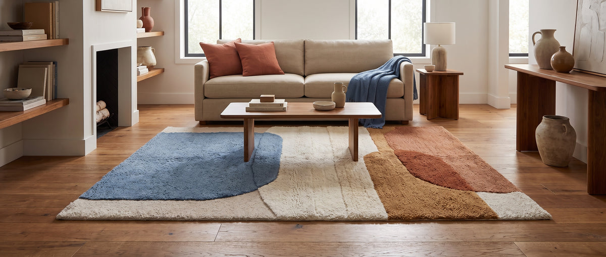 Sur un fond crème, ce tapis en laine tuftée présente des formes abstraites sculptées bleu et terracotta dans un salon