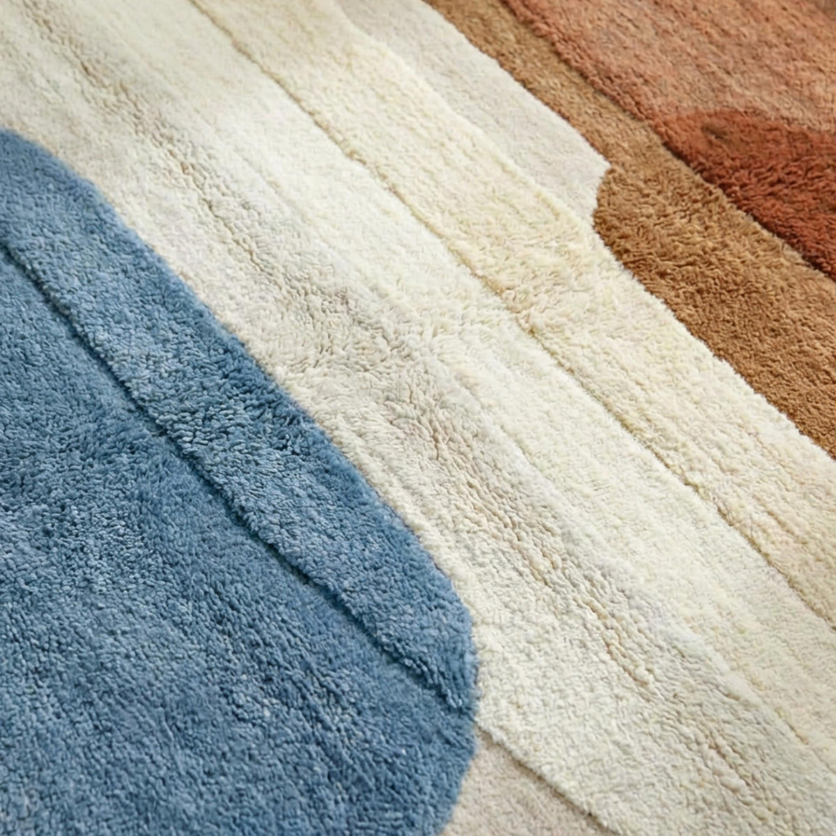 La texture épaisse et le relief sculpté des formes abstraites en laine tuftée bleu, crème et terracotta