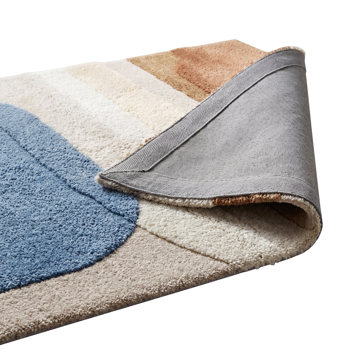 Le coin replié du tapis en laine tuftée et sculptée montre son envers tissé gris, son épaisseur et ses motifs colorés