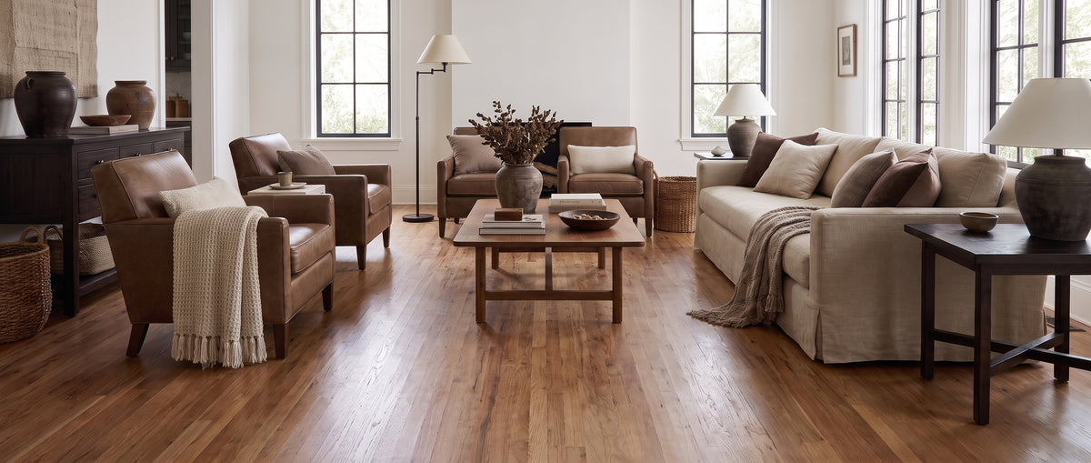 Lumineux salon au parquet clair, meublé de canapés et fauteuils en cuir et tissu, sans tapis sur le sol nu