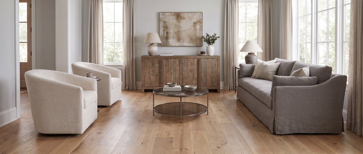 Un salon lumineux révèle son parquet clair sans tapis, meublé de fauteuils crème, d'un canapé gris et d'un buffet