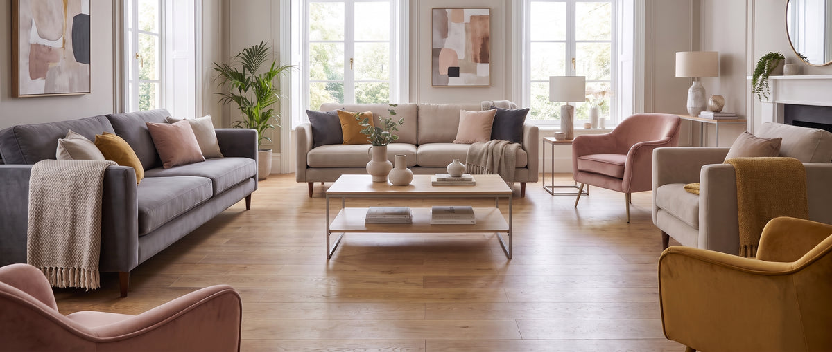 Vaste salon lumineux au parquet clair et sol nu, avec canapés gris et beiges, fauteuils roses et ocres, ambiance moderne