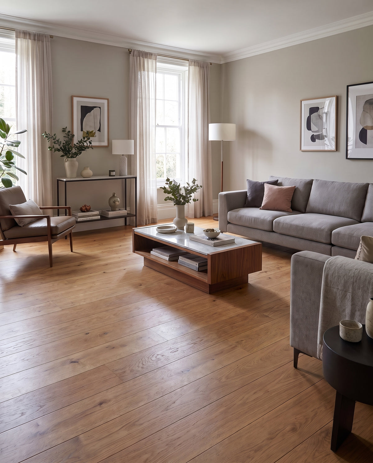 Parquet clair et sol nu dans un salon lumineux, avec canapés gris, fauteuil en cuir marron, table basse bois et marbre
