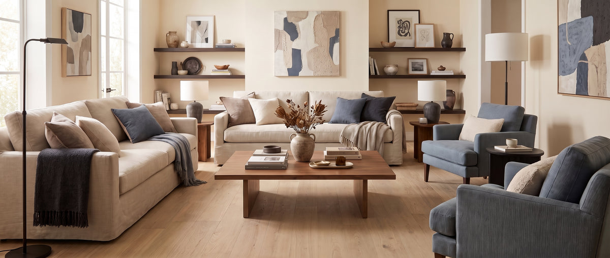 Canapés beiges et fauteuils bleus meublent ce salon au sol nu en parquet clair, avec étagères et décorations