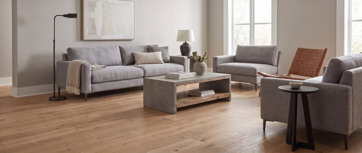 Pièce à vivre lumineuse au sol parqueté clair, meublée d'un grand canapé gris, de fauteuils et d'une table basse, sans tapis