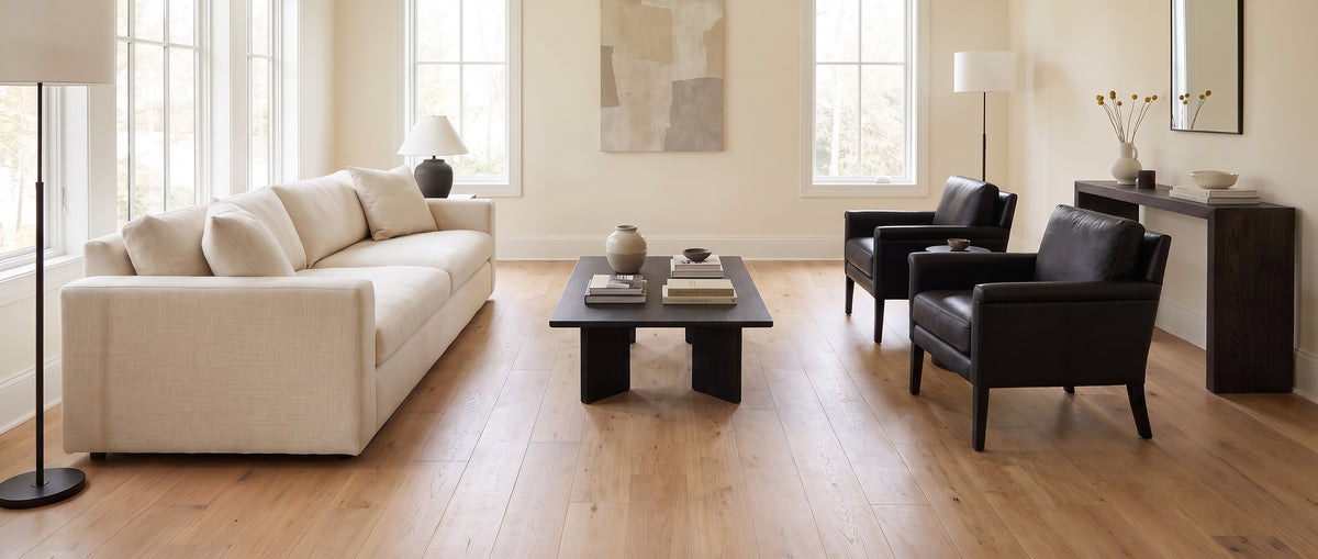 Pièce à vivre moderne, avec un sol en bois nu, un grand canapé clair, des fauteuils sombres et une table basse