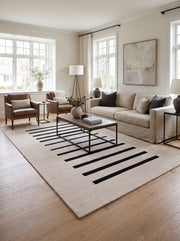 De grandes bandes noires sur un tapis rectangulaire en laine ivoire fait main, dans un salon lumineux