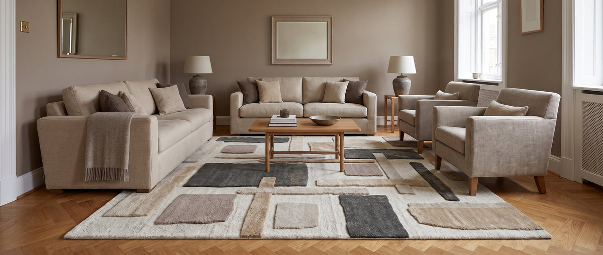 Avec sa surface sculptée, ce tapis en laine ivoire et taupe arbore des blocs sable, brun et anthracite dans un salon