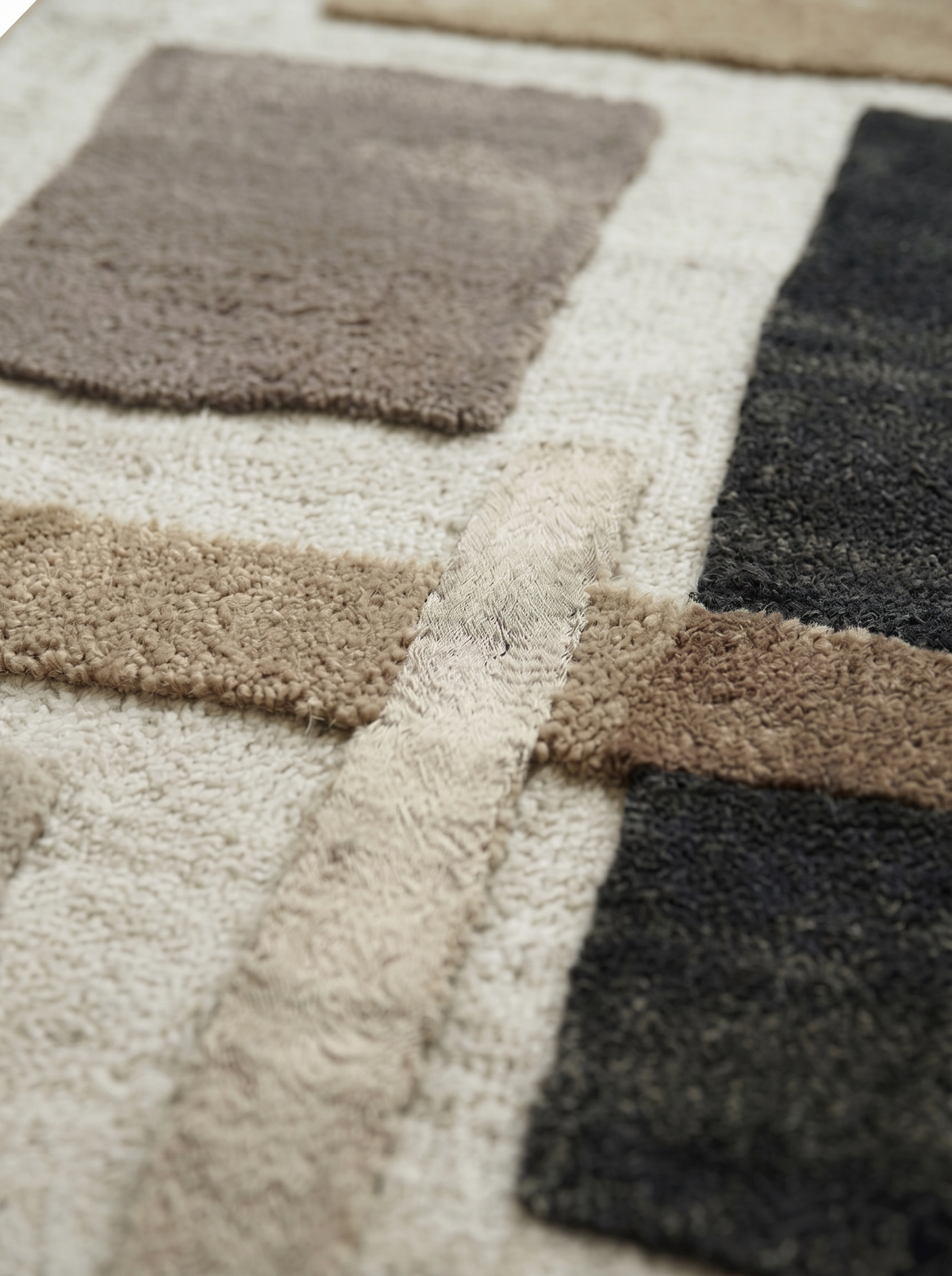 Le relief et la texture de la laine tuftée dessinent des blocs ivoire, sable, taupe et anthracite